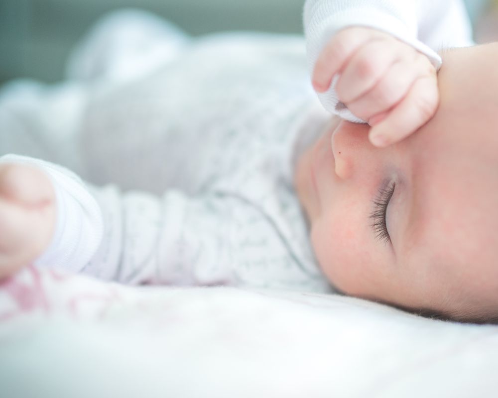 Sleepy baby in crib rubbing eye with her hand