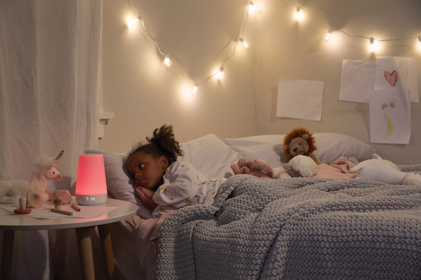 little girl in bed looking at toddler alarm clock