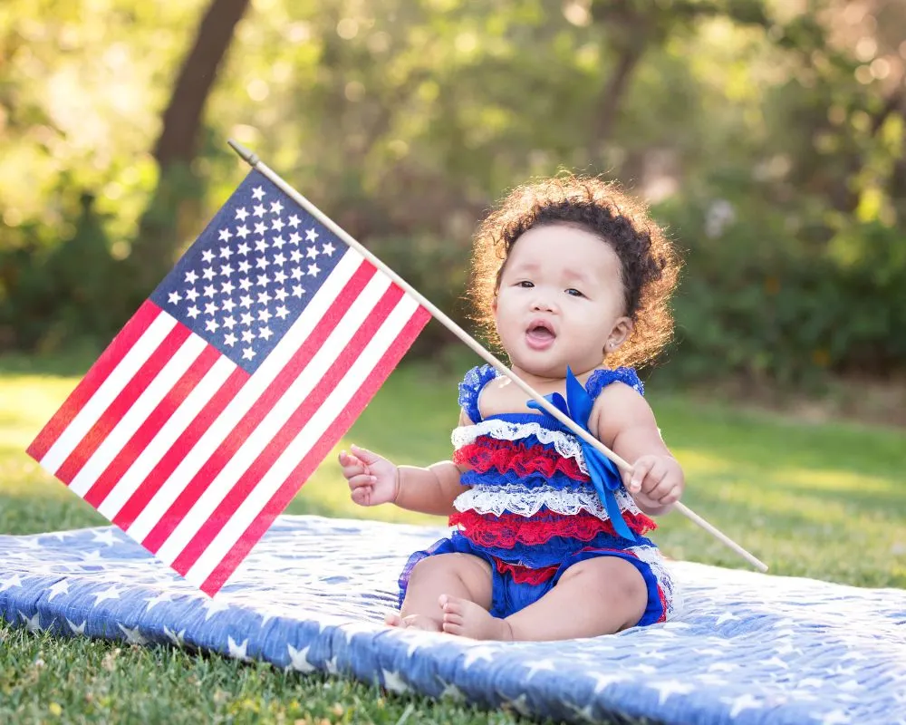 baby holding an American flag while sitting on a blanket