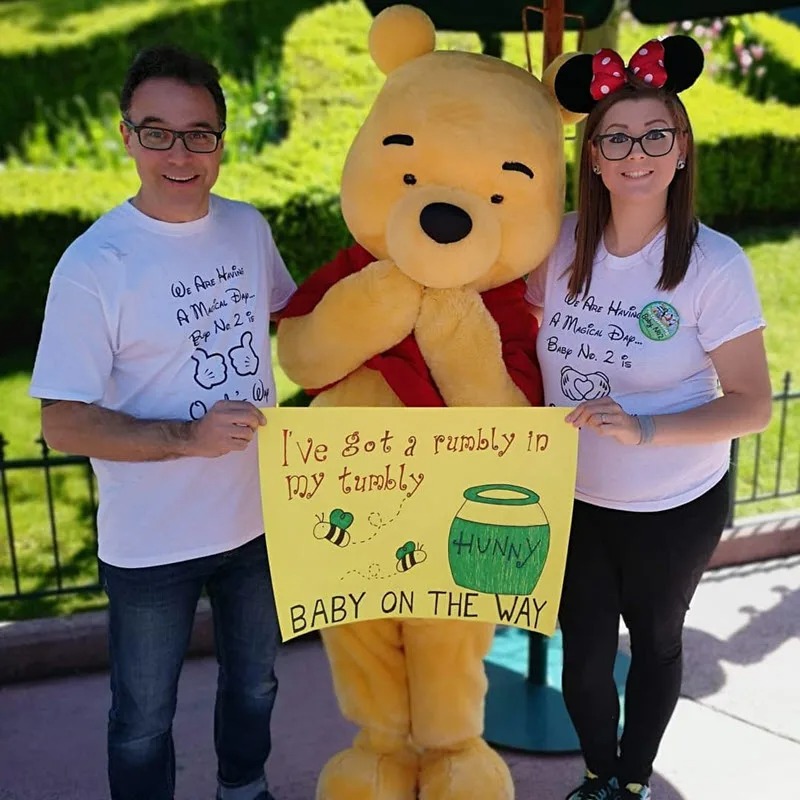 couple holding a sign to announce pregnancy with Pooh Bear