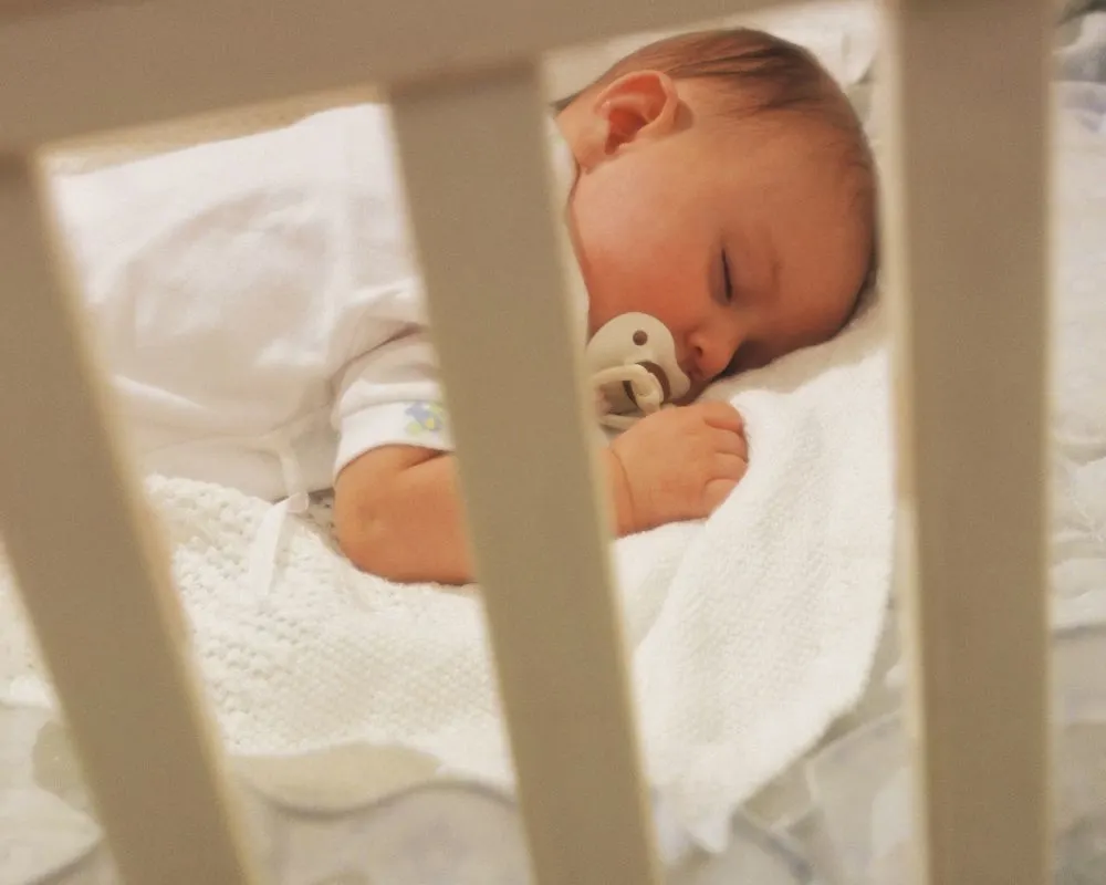 baby sleeping on his stomach in a crib with a pacifier in his mouth