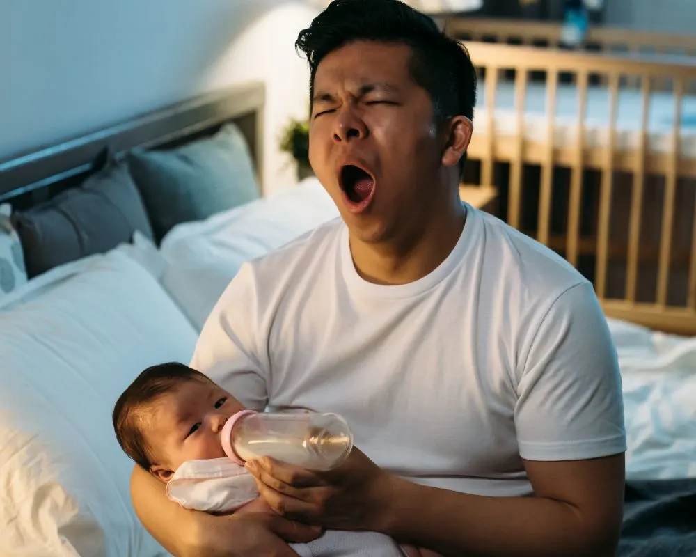 tired dad yawning and feeding baby in the middle of the night