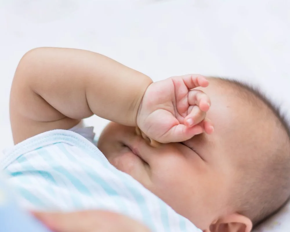 baby rubbing its face and arms showing a sleep cue