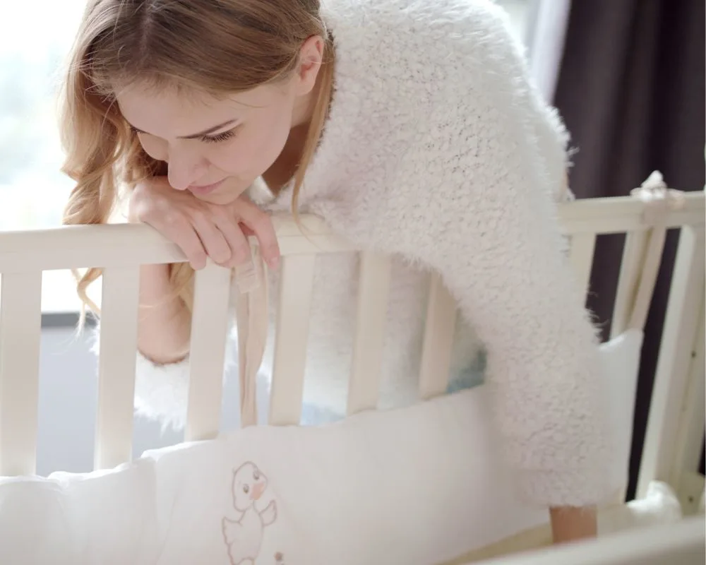 mother leaning over side crib to touch baby as part of soothing ladder