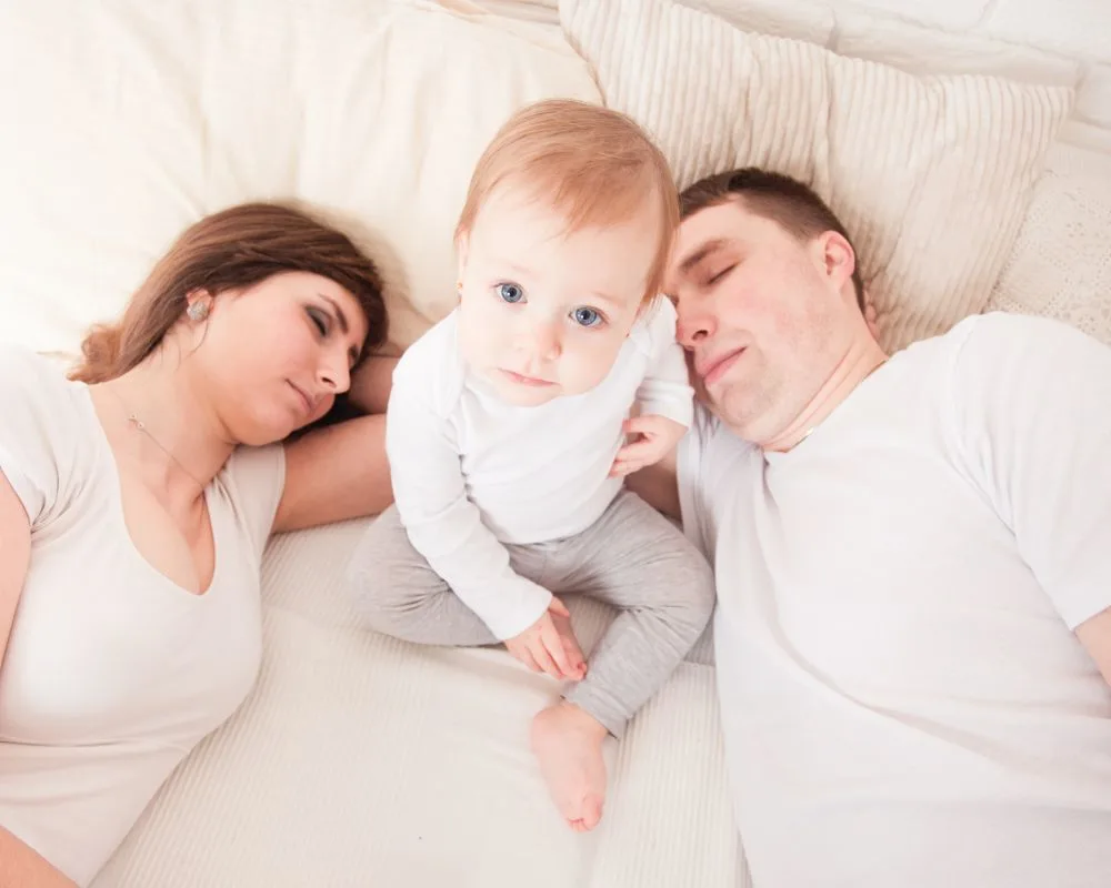 toddler sitting up awake while parents sleep