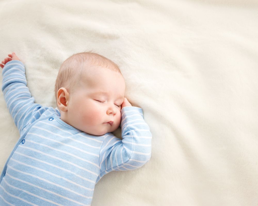 Baby sleeping in blue onesie.